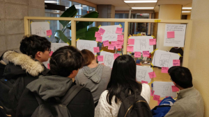 Groupe d'étudiants de dos regardant des post-its sur un mur vitré.